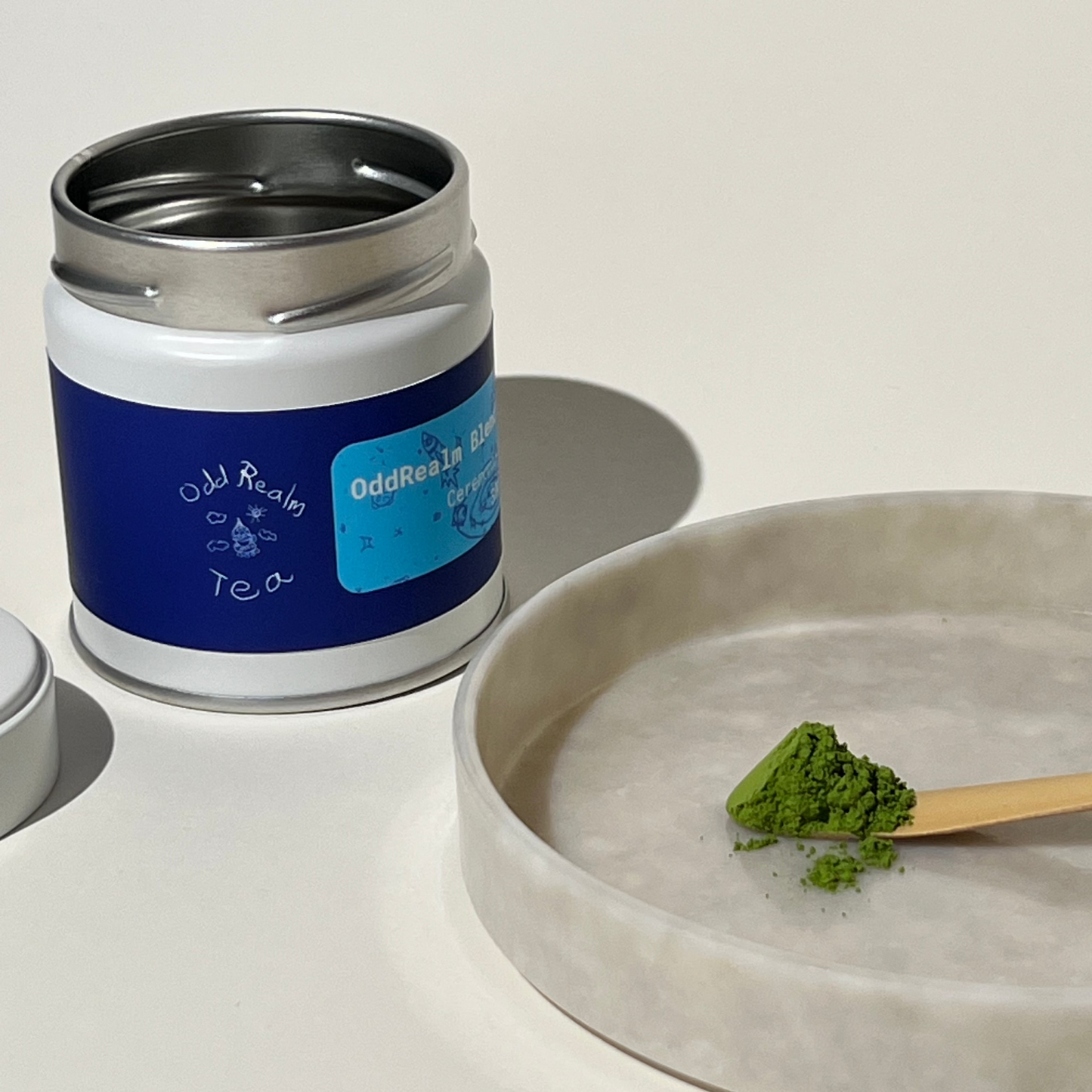OddRealm Blend Matcha No. 2 Aufnahme vom Pulver, im Hintergrund OddRealm Blend Matcha No. 2 Dose mit OddRealm Tea Logo