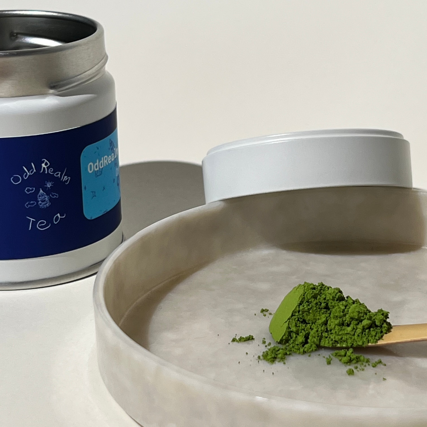 OddRealm Blend Matcha No. 2 Nahaufnahme vom tiefgrünen Pulver, im Hintergrund OddRealm Blend Matcha No. 2 Dose mit OddRealm Tea Logo